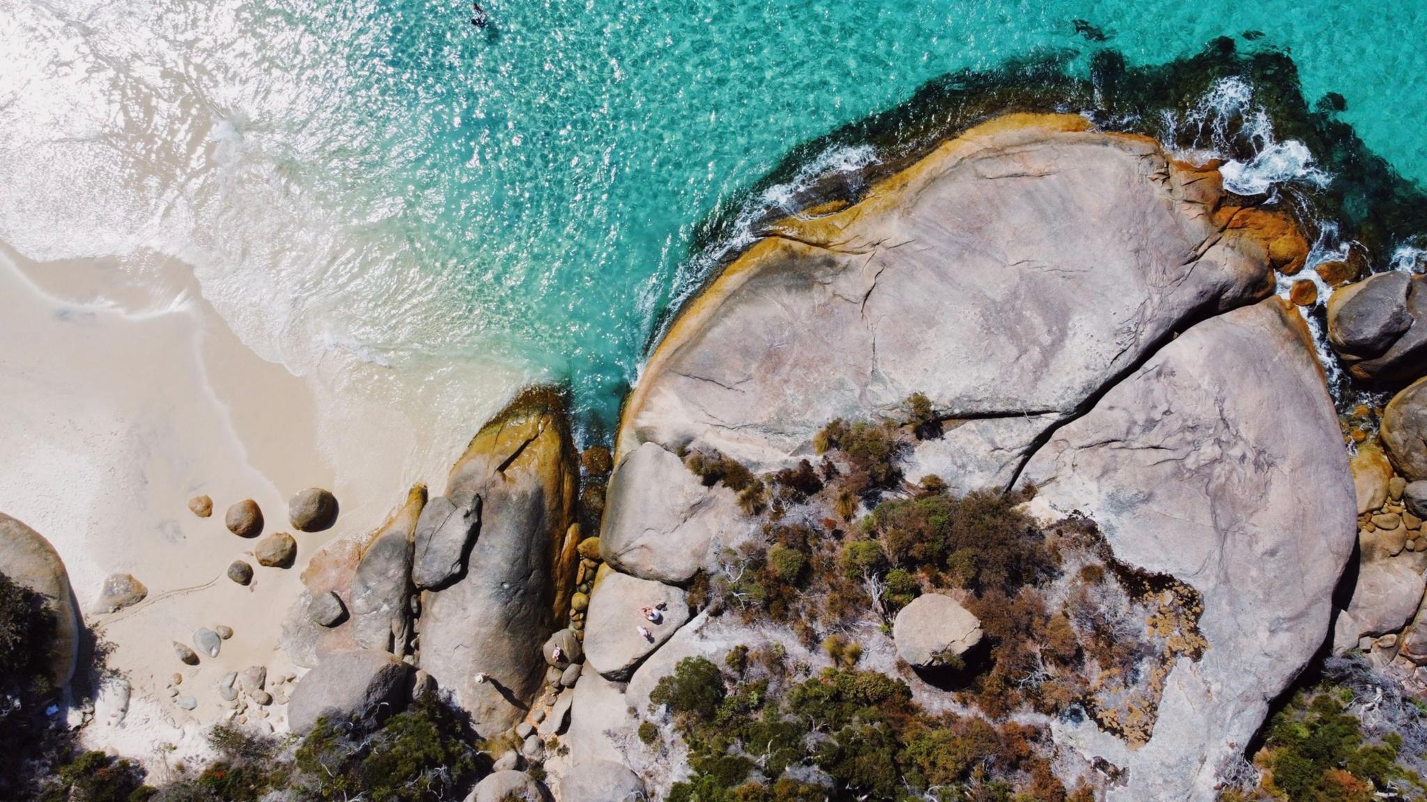 Aerial view of a coastal landscape featuring turquoise water, sandy beach, and large rock formations