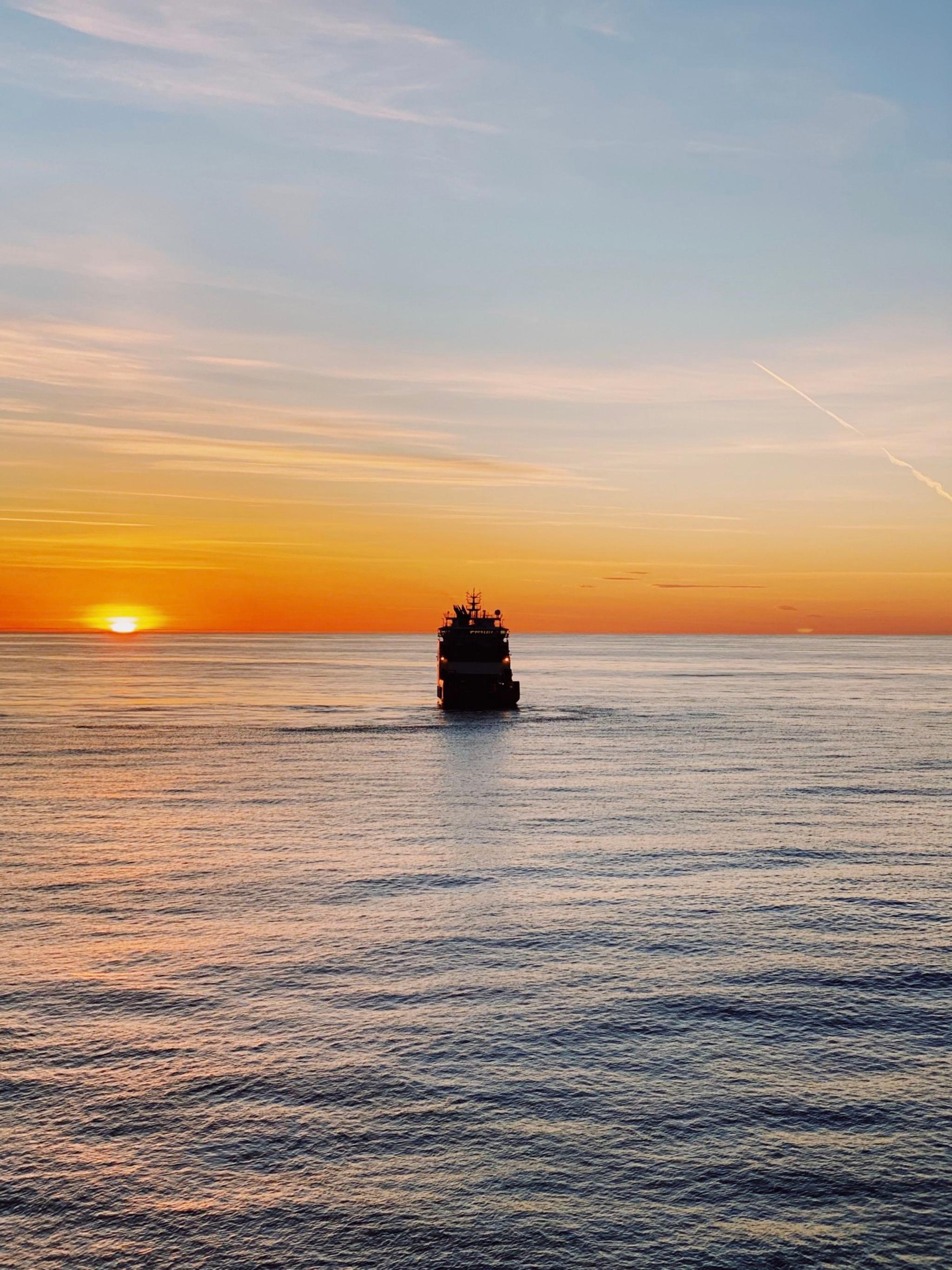 A ship sailing on calm waters during a vibrant sunset